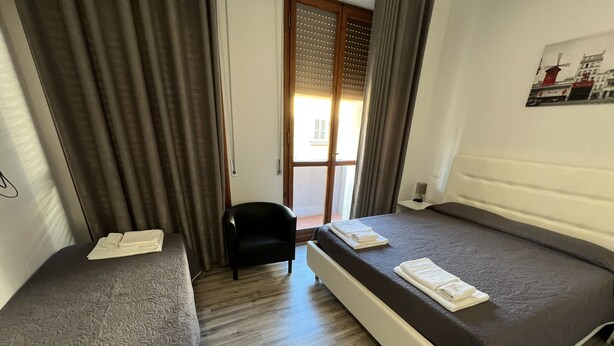 A hotel room with two single beds, a chair, a small table, and a window with blinds. - Affittacamere Umberto I (Foligno)