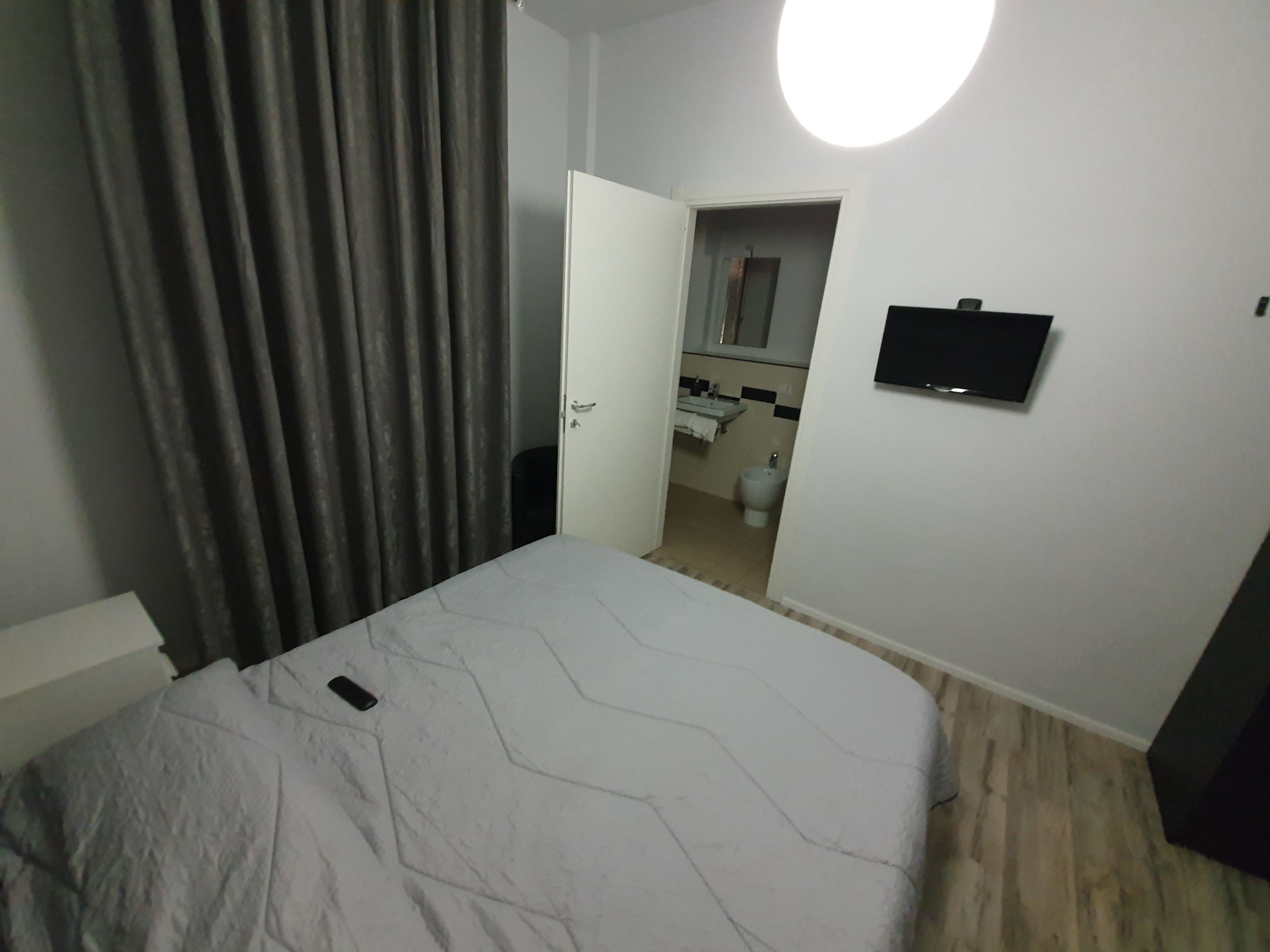 Quarto com cama, televisão e banheiro visível por uma porta aberta, além de cortina.