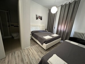 A modern hotel room with a large bed, a smaller bed, a bathroom with a shower, and a painting on the wall. - Affittacamere Umberto I (Foligno)