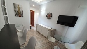 A modern living room with a dining area, a TV mounted on the wall, and a clock. - Affittacamere Umberto I (Foligno)