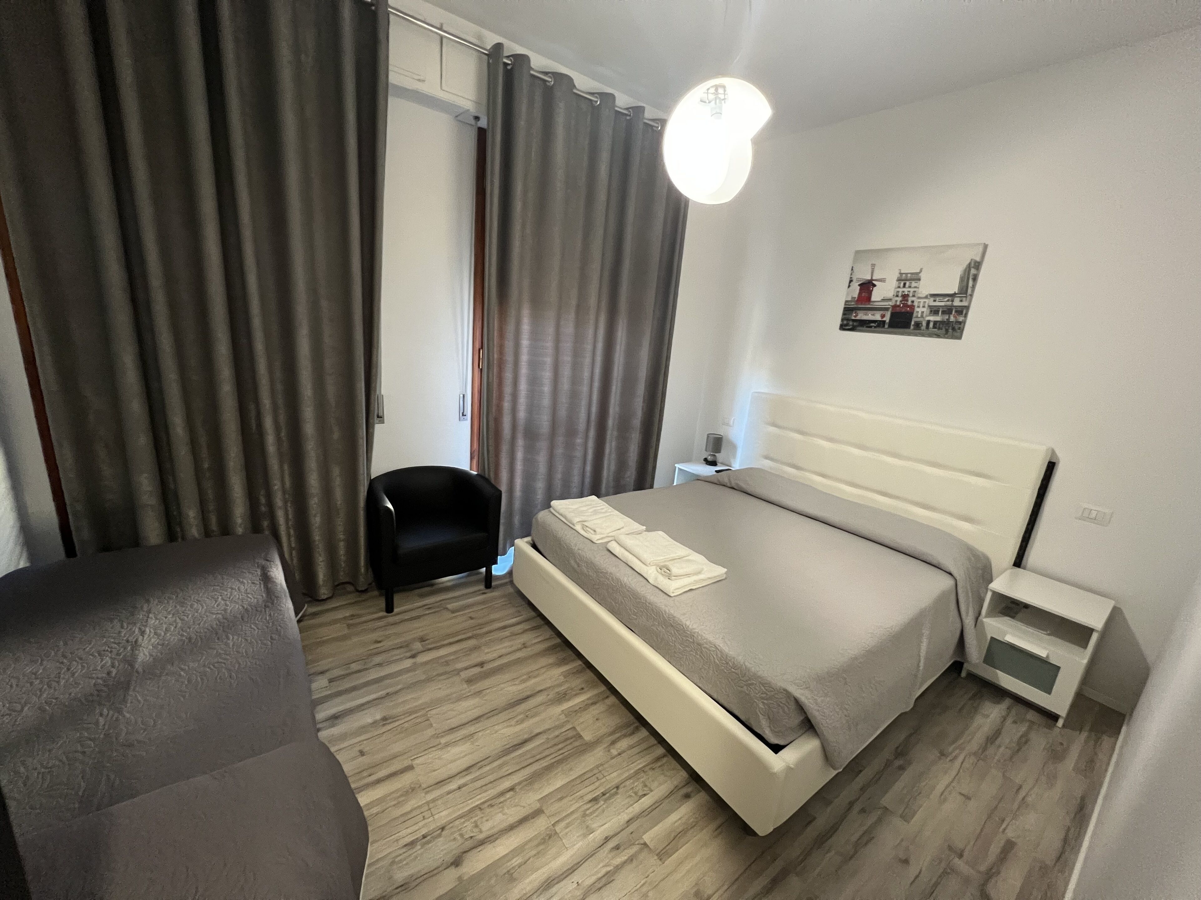 Ein modernes Hotelzimmer mit Bett, Sessel, Nachttisch und Wandleuchte.