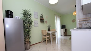 A compact kitchen with a refrigerator, a dining table with chairs, and a potted plant.