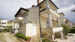 A two-story residential building with a balcony, a staircase, and a garden area.