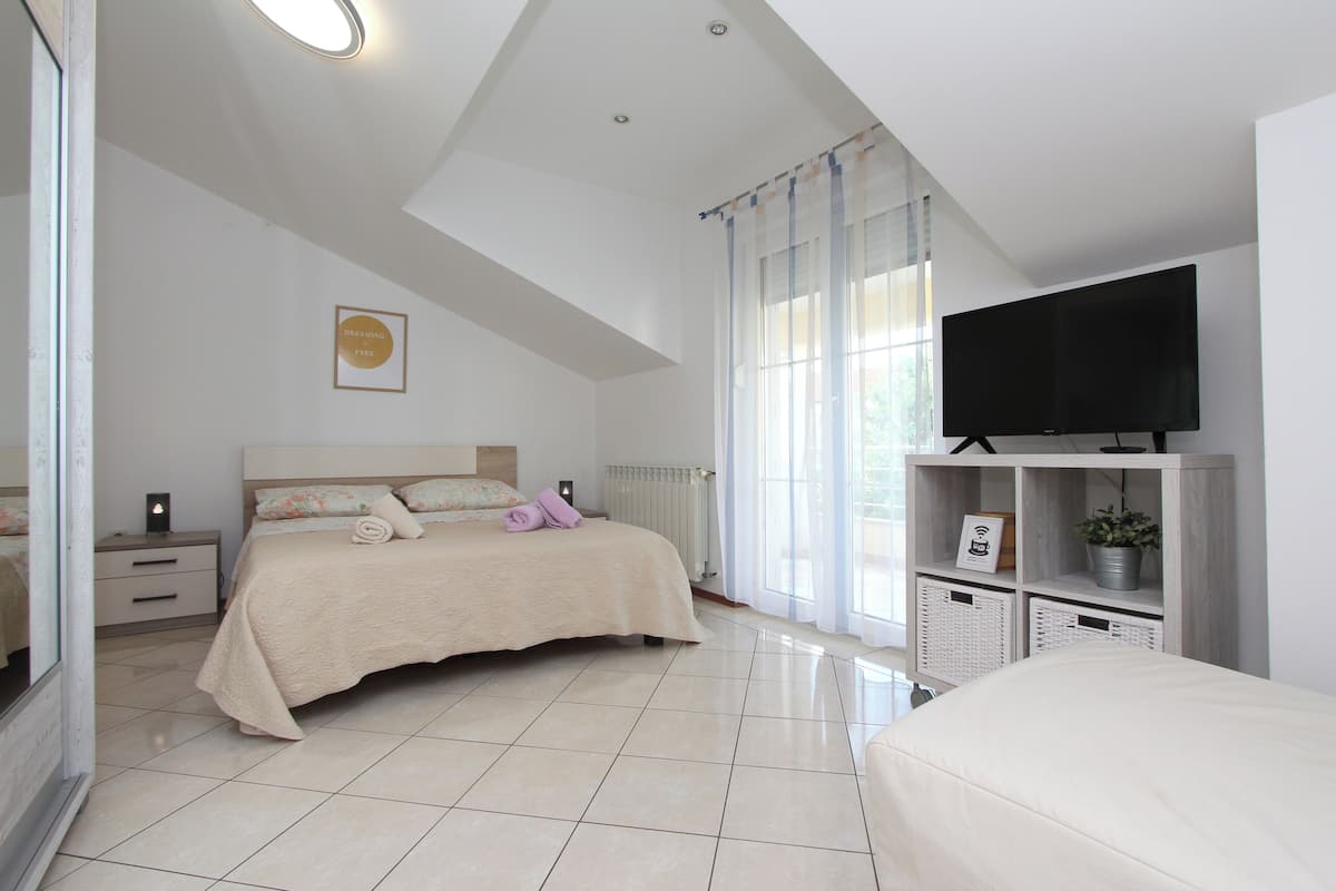 Un dormitorio con cama, televisor, mesita de noche y ventana con cortinas.