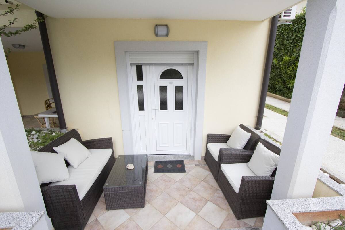 Un patio con dos sofás de mimbre oscuro, una mesita y una puerta blanca.