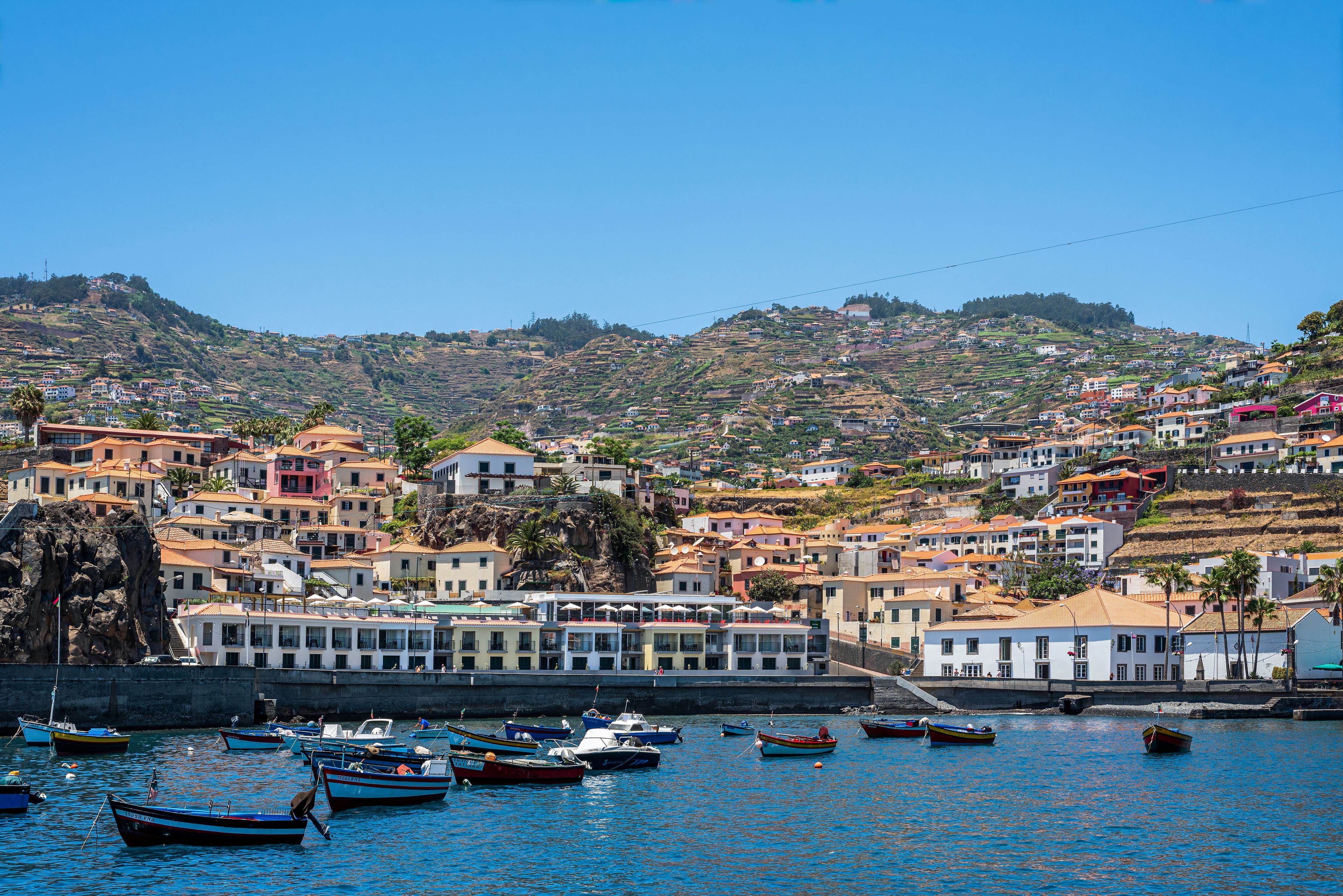 Un pueblo costero con casas escalonadas, un puerto con barcos y un cielo azul despejado.