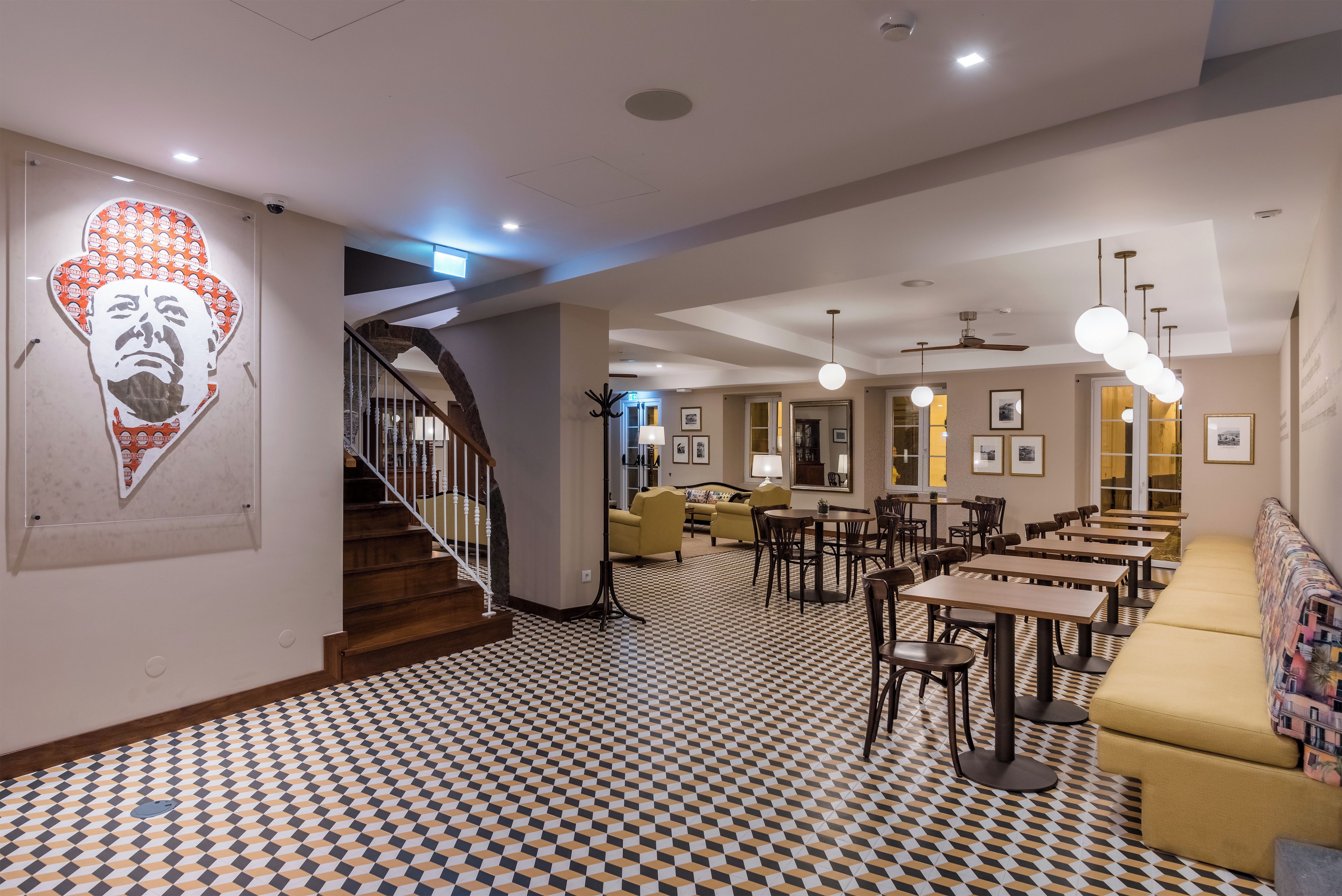 A hotel lobby with a checkered floor, a staircase, and a seating area with tables and chairs.