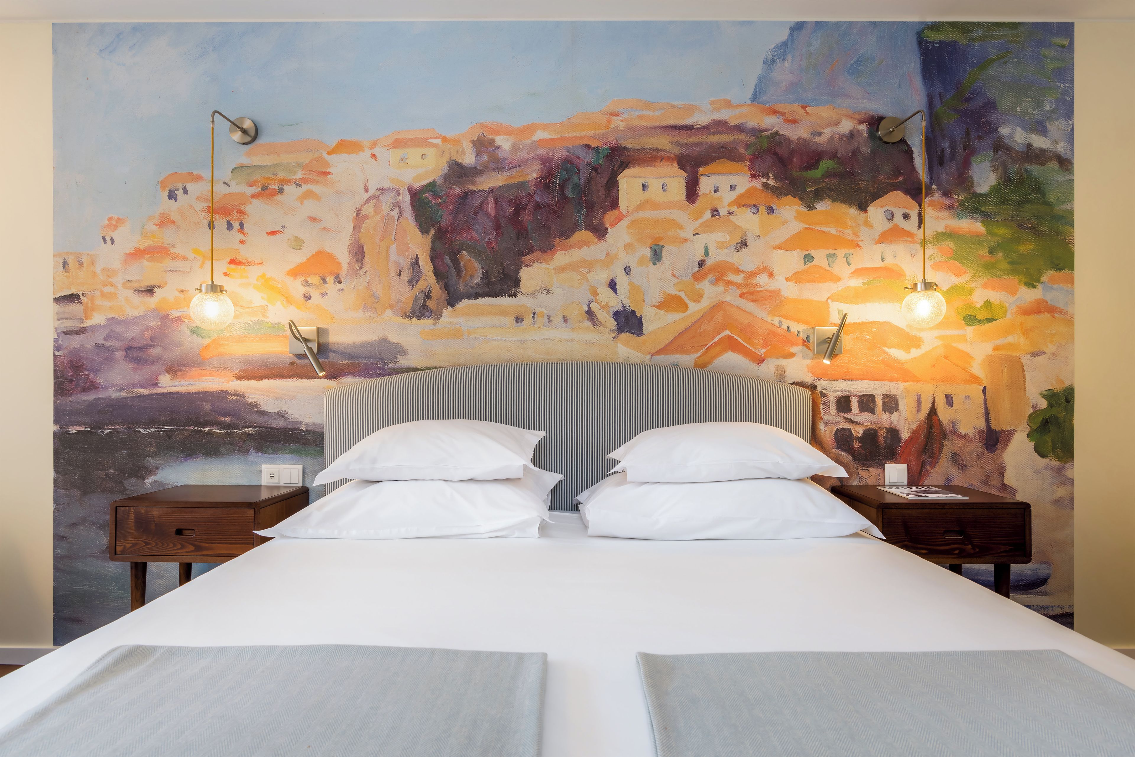 A hotel room with a bed, two bedside tables, and a large painting on the wall.