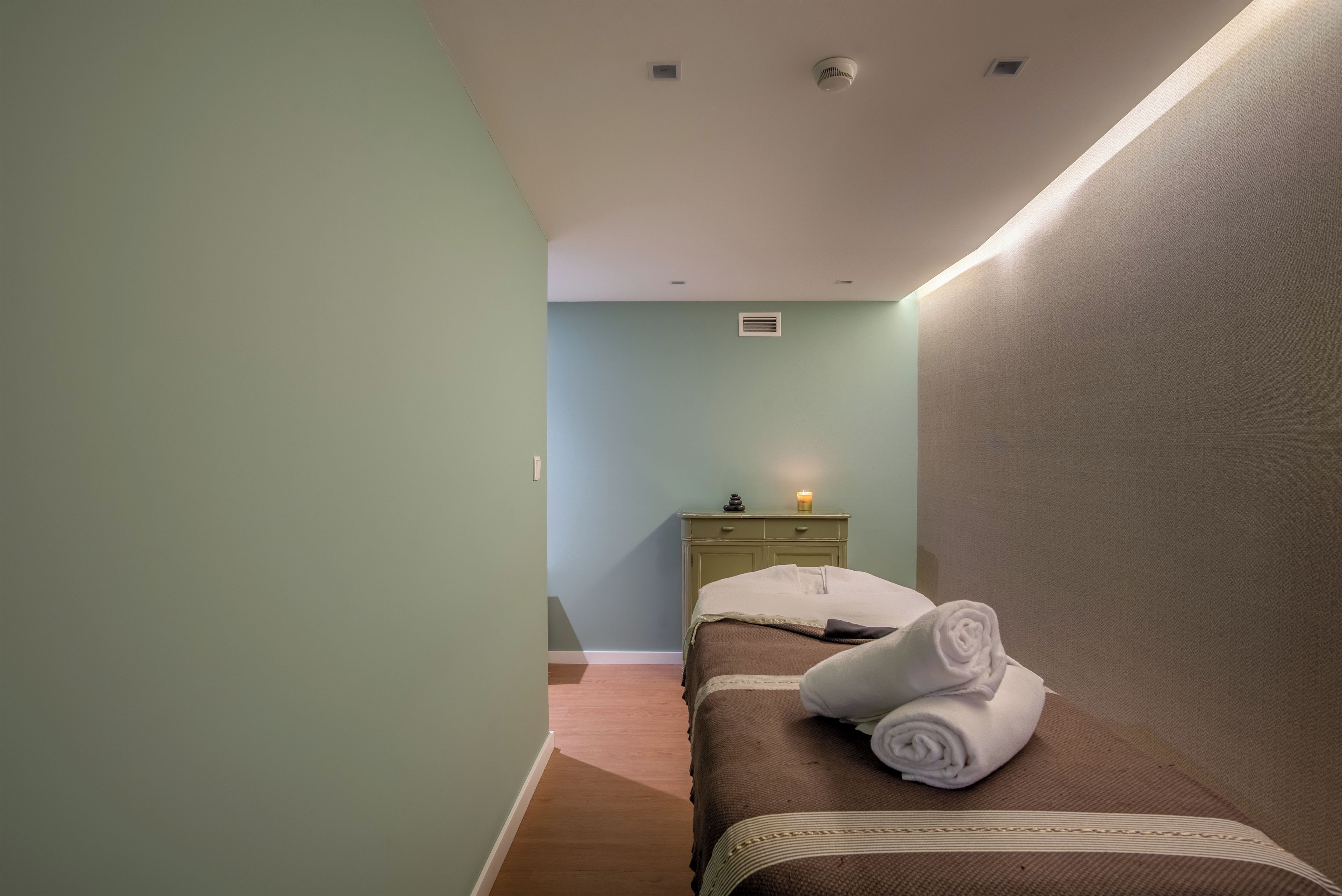 Un dormitorio con una cama individual, una mesita de noche, un calentador de pared y un ventanal pequeño.