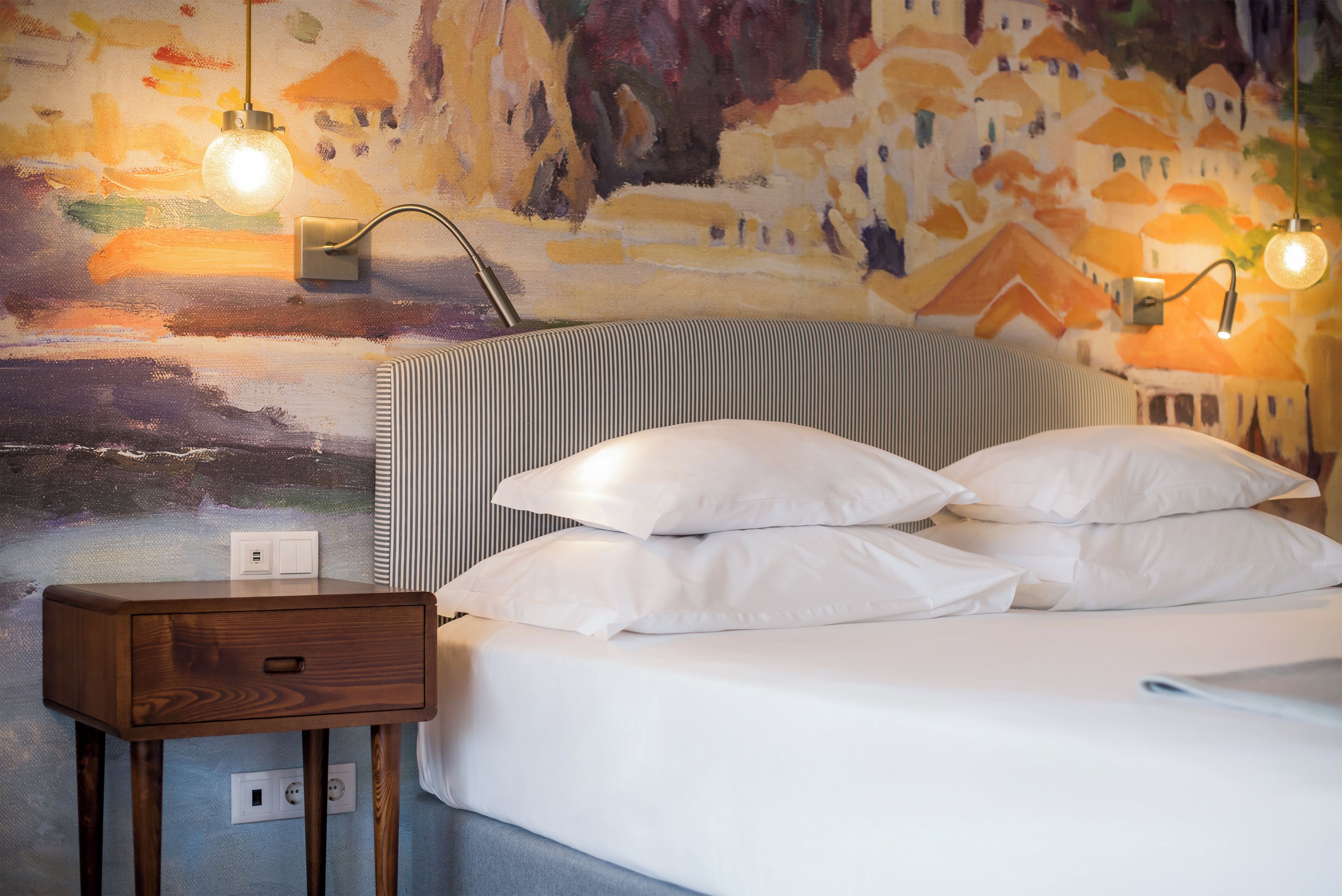 Een bed met witte lakens, een gestreept hoofdbord en twee bedlampen.