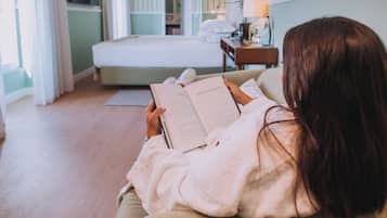 Eine Person liest ein Buch in einem Zimmer mit einem Bett, einem Nachttisch und einer Lampe.