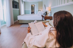 Una persona leyendo un libro en una habitación con cama, mesita de noche y lámpara.