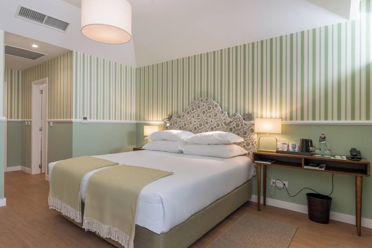 A neatly arranged bedroom with a bed, bedside lamps, a desk, and a trash bin.