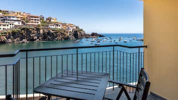 A balcony with a table and chairs overlooking a coastal area with boats and buildings.