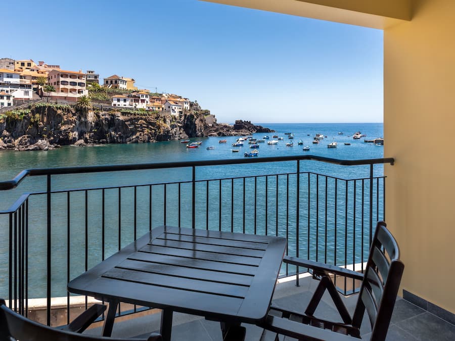 A balcony with a table and chairs overlooking a coastal area with boats and buildings.