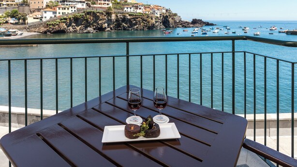 Une table avec un dessert et deux verres de vin rouge, donnant sur une ville côtière avec des bateaux et des bâtiments.