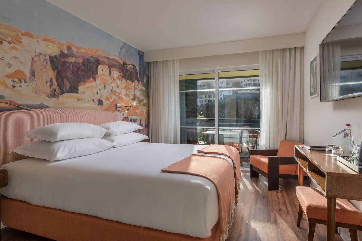A hotel room with a large bed, a desk, a chair, a TV, and a window with curtains.