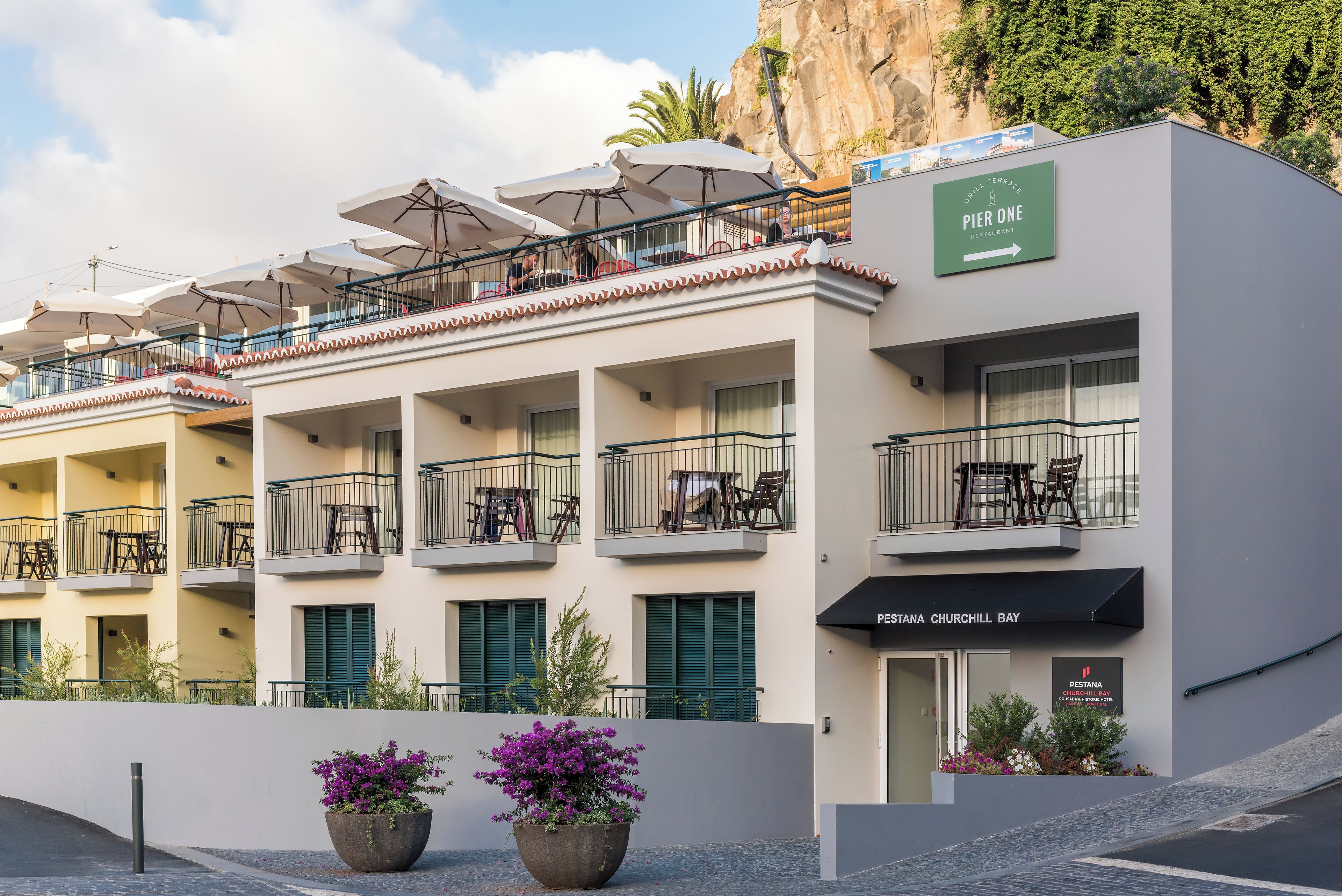 A hotel with multiple balconies, outdoor seating, and a sign for a restaurant.