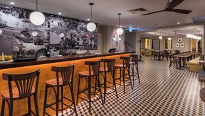 Un espace bar avec un sol à carreaux, des tabourets de bar et une fresque murale.