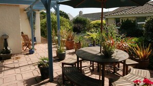 A patio with a round wooden table, chairs, and a large umbrella. There are potted plants and a pergola structure. - Anchors Away - One Bedroom Cottage, Sleeps 2 (Downderry)