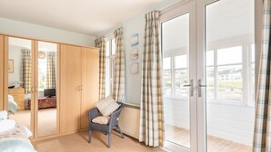 Een slaapkamer met een kledingkast, een stoel, een bed en een groot raam met gordijnen.