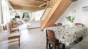 Amplia sala de estar con una escalera de madera, una mesa de comedor con mantel estampado de pájaros y vistas al exterior.