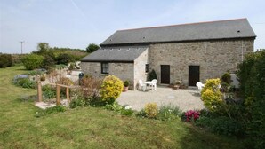 A stone building with a sloped roof, a fenced garden area with various plants, and outdoor seating. - Tom Thumb - One Bedroom Cottage, Sleeps 2 (Mabe Burnthouse)
