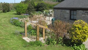 A stone house with a sloped roof, surrounded by a well-maintained garden with various plants and a wooden fence. - Tom Thumb - One Bedroom Cottage, Sleeps 2 (Mabe Burnthouse)