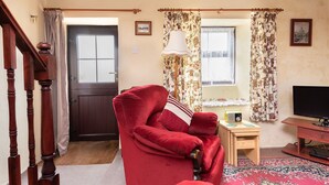 A cozy living room with a red armchair, a wooden table with a radio, and a television on a wooden stand. - Tom Thumb - One Bedroom Cottage, Sleeps 2 (Mabe Burnthouse)