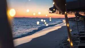 Vista de la playa con un atardecer, un muelle y luces colgantes.