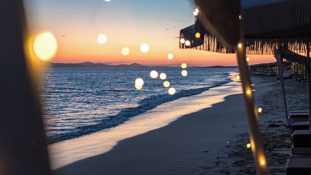 A beach view with a sunset, a pier, and string lights. - Glaronissi Beach (Naxos)