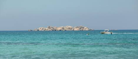 A calm sea with a rocky island in the distance and a speedboat in the foreground.
