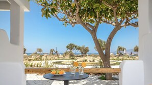 A table with a plate of fruit and glasses, overlooking a scenic landscape with a tree and a view of the sea. - Glaronissi Beach (Naxos)
