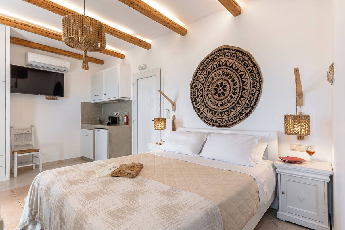 A bedroom with a large bed, bedside tables, a wall-mounted tapestry, and a kitchen area with cabinets and a stove.