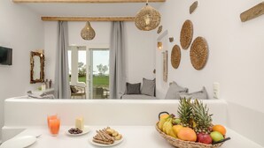 A modern room with a white sofa, a dining table with breakfast items, and a view of the outdoors. - Glaronissi Beach (Naxos)