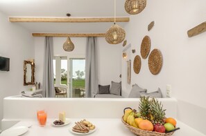 A modern room with a white sofa, a dining table with breakfast items, and a view of the outdoors. - Glaronissi Beach (Naxos)