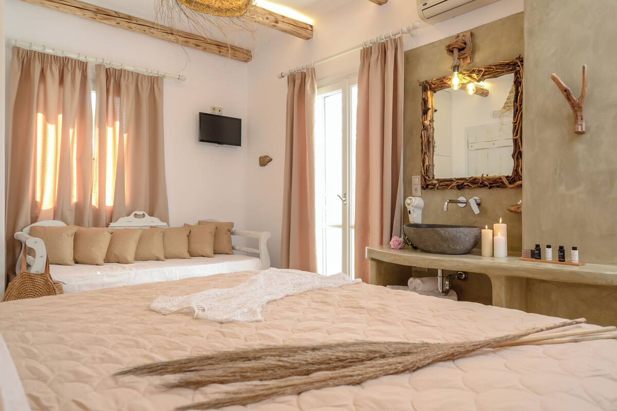 A bedroom with a large bed, a bedside table with a bowl sink, a mirror, and a television on the wall.