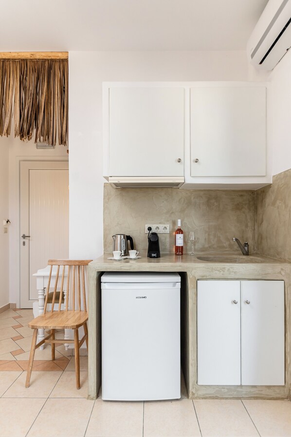 A compact kitchen with white cabinets, a small refrigerator, a coffee maker, and a wine bottle. - Glaronissi Beach (Naxos)