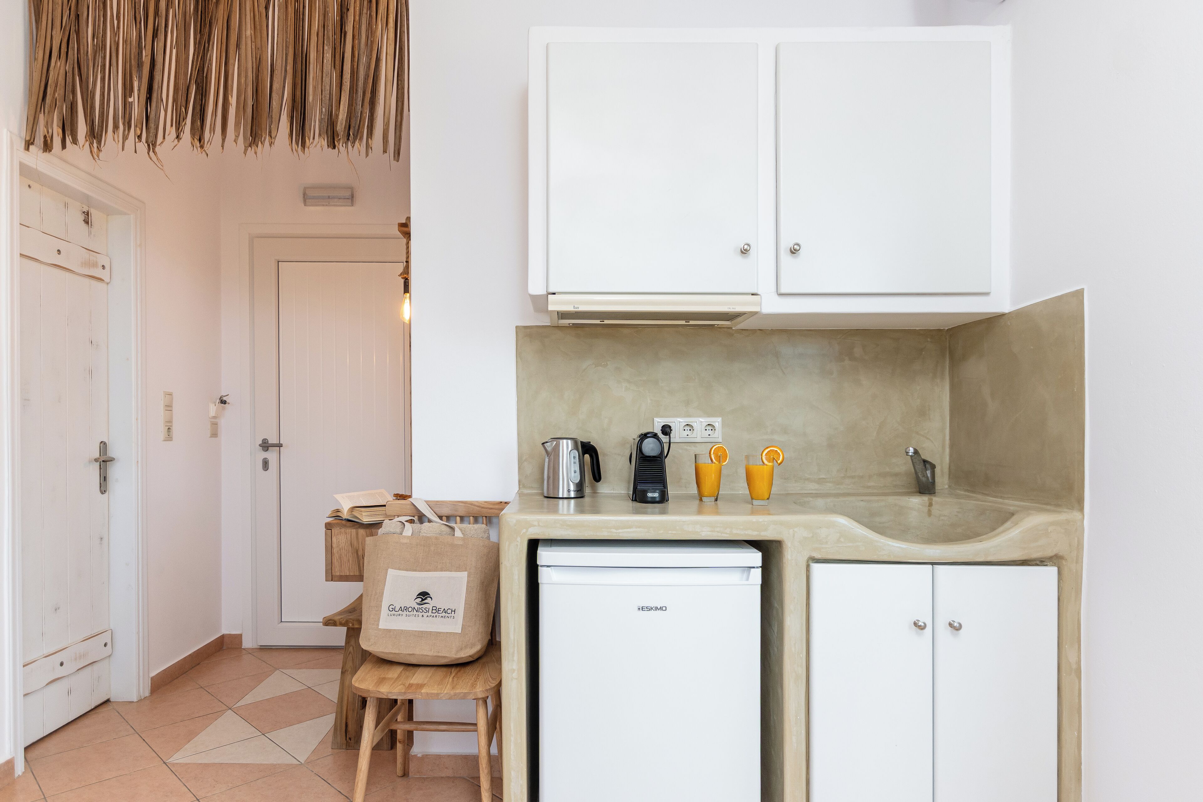 A compact kitchen with white cabinets, a small refrigerator, a coffee maker, and a kettle on the countertop.