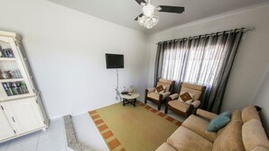 A living room with a sofa, chairs, a coffee table, a cabinet, and a ceiling fan. - Casa Terceira avenida - 10 pessoas (Itapema)