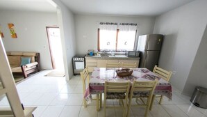 A compact kitchen with a dining table, chairs, a refrigerator, and a microwave. - Casa Terceira avenida - 10 pessoas (Itapema)