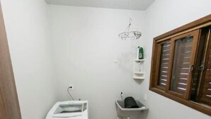 A small, white-walled room with a washing machine, a sink, and a window with blinds. - Casa Terceira avenida - 10 pessoas (Itapema)