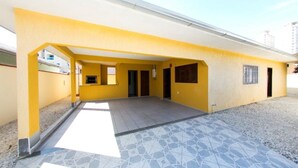 A yellow building with a covered patio area and tiled flooring. - Casa Terceira avenida - 10 pessoas (Itapema)
