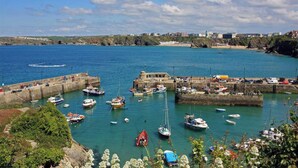 Un port côtier où sont amarrés de nombreux bateaux, avec une jetée en pierre et des bâtiments en arrière-plan.
