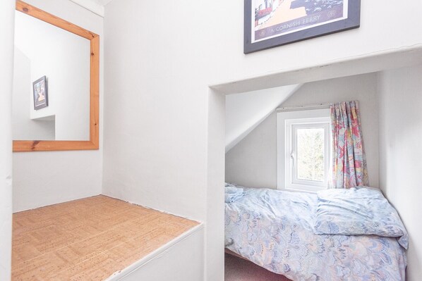 Een slaapkamer met een bed, een raam met gordijnen, een houten hoofdeinde en een lijst met een foto aan de muur.