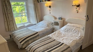 Ein Schlafzimmer mit zwei Betten, einem Fenster mit Vorhängen, Nachttischlampen und einem kleinen Nachttisch mit einem Radio.