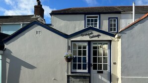 Ein Cottage namens 'Crumpet Cottage' mit einer weißen Fassade, einer blauen Tür und einem kleinen Steinschritt zum Eingang.