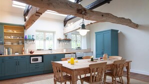 A kitchen with wooden beams, teal cabinets, and a dining table with chairs. - Carneggan Barn - Three Bedroom Cottage, Sleeps 6 (Lanteglos)
