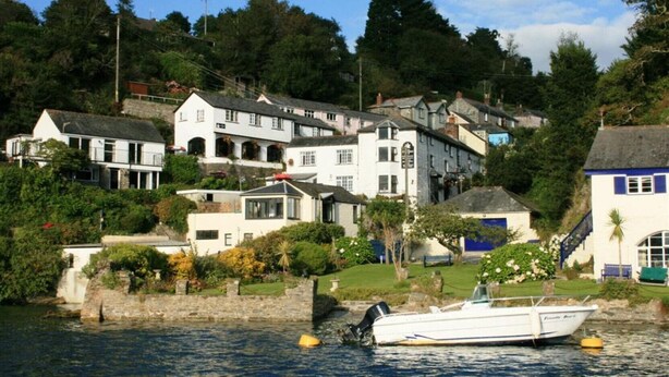 A coastal town with houses along the water, a boat docked near the shore, and a stone wall. - Carneggan Barn - Three Bedroom Cottage, Sleeps 6 (Lanteglos)