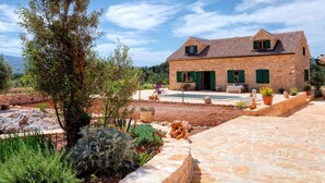 A stone house with a tiled roof, a swimming pool, and a garden with various plants and a large tree. - Stunning Renovated Traditional Stone Villa, Private Pool & Mountain Views just 800 m from the Sea! (Stari Grad)